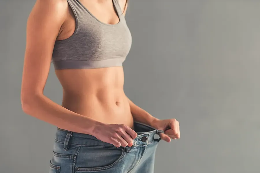 Abdominal-Weight-Loss-Clinic A woman who has lost weight holds her jeans away from her waist. Schedule abdominal weight loss treatment from Nonkulie Dladla, M.D. in Manhattan.