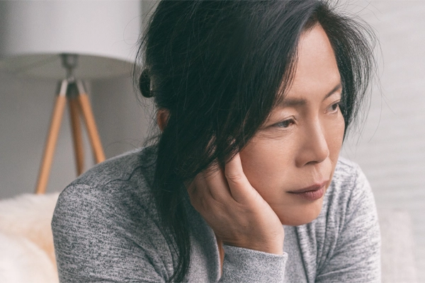 Adrenal-Fatigue-Doctor A middle-aged asian woman sitting on her couch, resting her head on her hand, suffering from adrenal fatigue. Get treatment for adrenal fatigue syndrome from Nonkulie Dladla, M.D. in Manhattan.