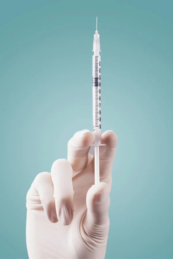 Aesthetic-Fillers-Treatment Close-up of a white-gloved hand holding a syringe against a light blue background, representing aesthetic filler services from Nonkulie Dladla, M.D. in Manhattan.