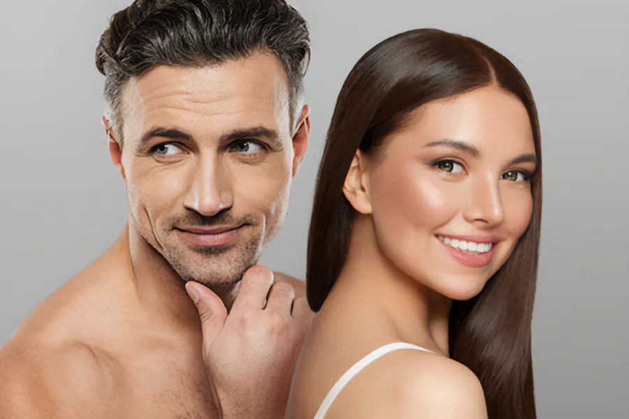 Aesthetics-Cosmetics-Doctor A handsome man and beautiful brunette woman stand against a gray background showing their smooth beautiful skin resulting from aesthetic and cosmetic care from Nonkulie Dladla, M.D. in Manhattan.