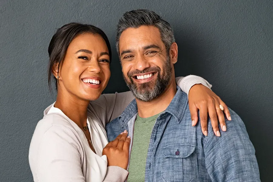 Bioidentical-Hormone-Therapy-Doctor A middle-aged couple with their arms around each other standing against a gray background and smiling, happy with the bioidentical hormone therapy they received from Nonkulie Dladla, M.D. in Manhattan.
