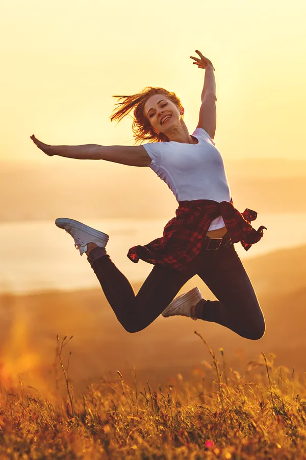 Breathwork-Treatment A woman happily jumps in the air in a field. Get breathwork treatment from Nonkulie Dladla, M.D. in Manhattan.