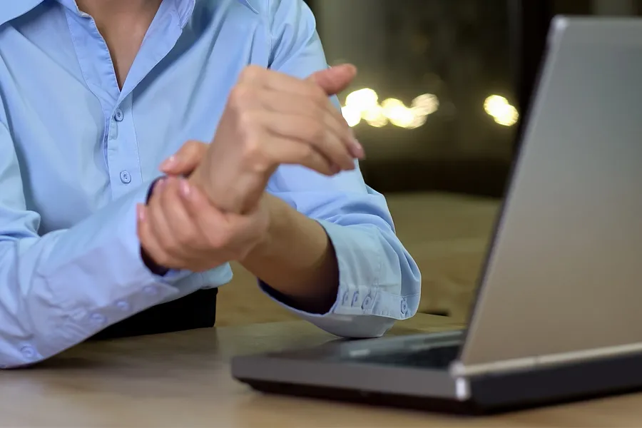 Carpal-Tunnel-Syndrome-Clinic A woman sits in front of her computer rubbing her hand in pain. Schedule treatment for carpal tunnel syndrome from Nonkulie Dladla, M.D. in Manhattan.