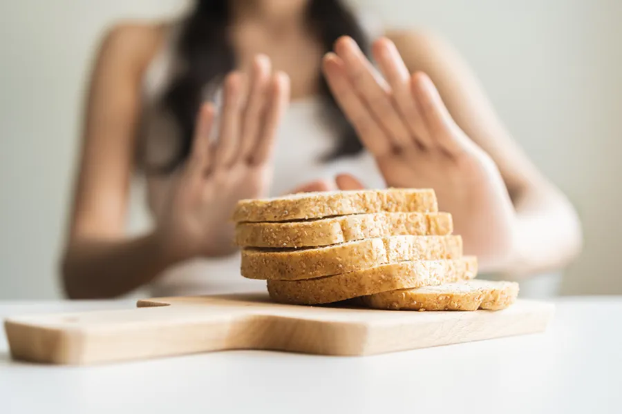 Celiac-Disease-Clinic Close up of a stack of bread slices on a cutting board with a woman's hands behind them, refusing to eat. Get treatment for Celiac Disease from Nonkulie Dladla, M.D. in Manhattan.