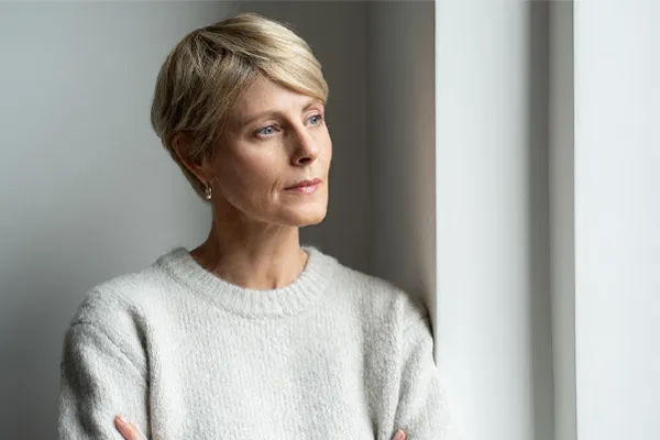 Chronic-Fatigue-Therapy A blond, middle-aged woman looks out the window with a tired expression. Get chronic fatigue treatment from Nonkulie Dladla, M.D. in Manhattan.