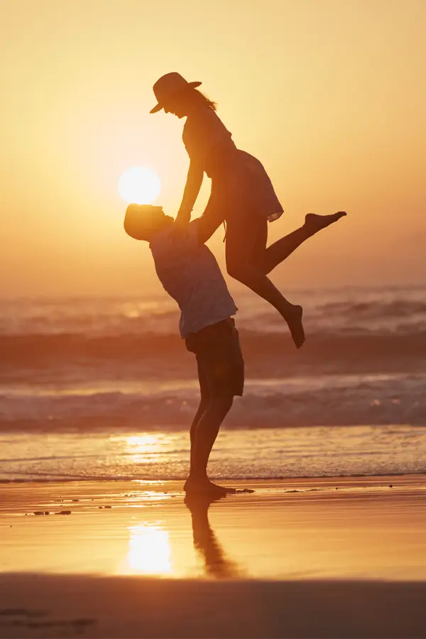 Glutathione-IV-Treatment A man holds his wife in the air on the beach at sunset. Get glutathione IV therapy from Nonkulie Dladla, M.D. in Manhattan.