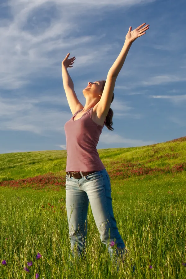 Graves-Disease-Treatment A woman in a tank top and jeans looks up with her arms outstretched to the sky in a field after successful treatment for Grave's Disease from Nonkulie Dladla, M.D. in Manhattan.