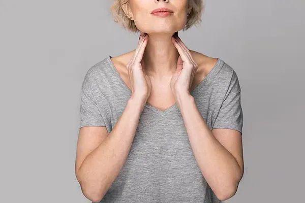 Hashimotos-Thyroiditis-Doctor An older blonde woman in a gray t-shirt holds her hands to her neck checking for signs of thyroid problems. Get help for Hashimoto's Thyroiditis from Nonkulie Dladla, M.D. in Manhattan.