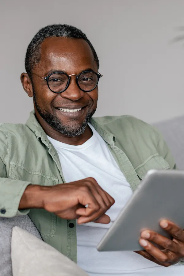 Kailo-Mindset-Therapy-Treatment A middle-aged Black man happily works on a tablet on his couch. Get Kailo Mindset Therapy from Nonkulie Dladla, M.D. in Manhattan.