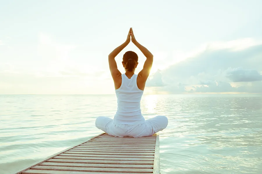 Kailo-Movement-Medicine-Clinic A woman doing yoga on a pier by the ocean. Schedule Kailo Movement Medicine treatment from Nonkulie Dladla, M.D. in Manhattan.