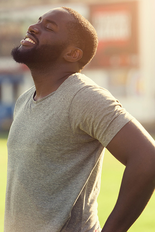 Lean-Muscle-and-Recovery-Treatment A black man in a gray t-shirt and smiles, looking up with closed eyes after a satisfying workout. Get treatment for lean muscle loss and recovery from Nonkulie Dladla, M.D. in Manhattan.
