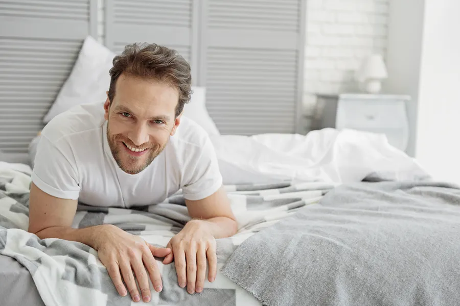 Low-Libido-in-Men-Doctor A dirty-blonde haired man lays on his stomach in bed smiling. Schedule treatment for low libido in men from Nonkulie Dladla, M.D. in Manhattan.