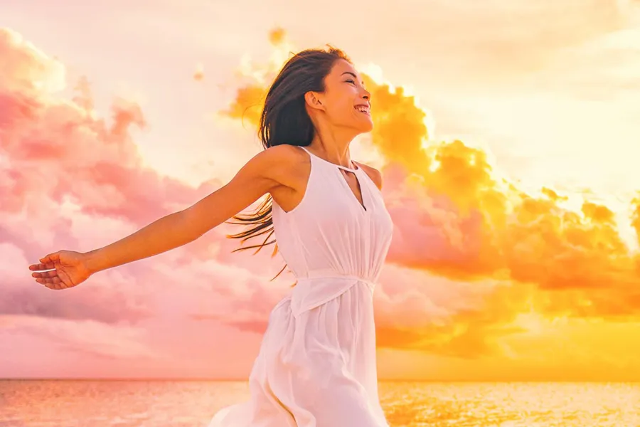 Myers-Cocktail-Clinic A woman in a thin white dress stretches out her arms joyously on the beach at sunrise. Get the Myers Cocktail IV treatment from Nonkulie Dladla, M.D. in Manhattan.