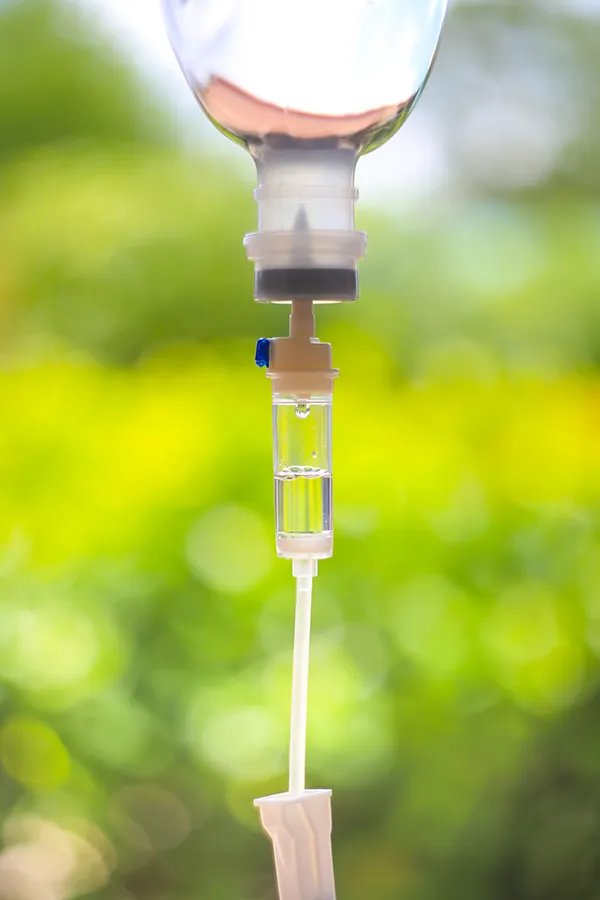 Myers-Cocktail-Treatment Close-up of an IV drip against a forest background. Get the Myers Cocktail IV treatment from Nonkulie Dladla, M.D. in Manhattan.