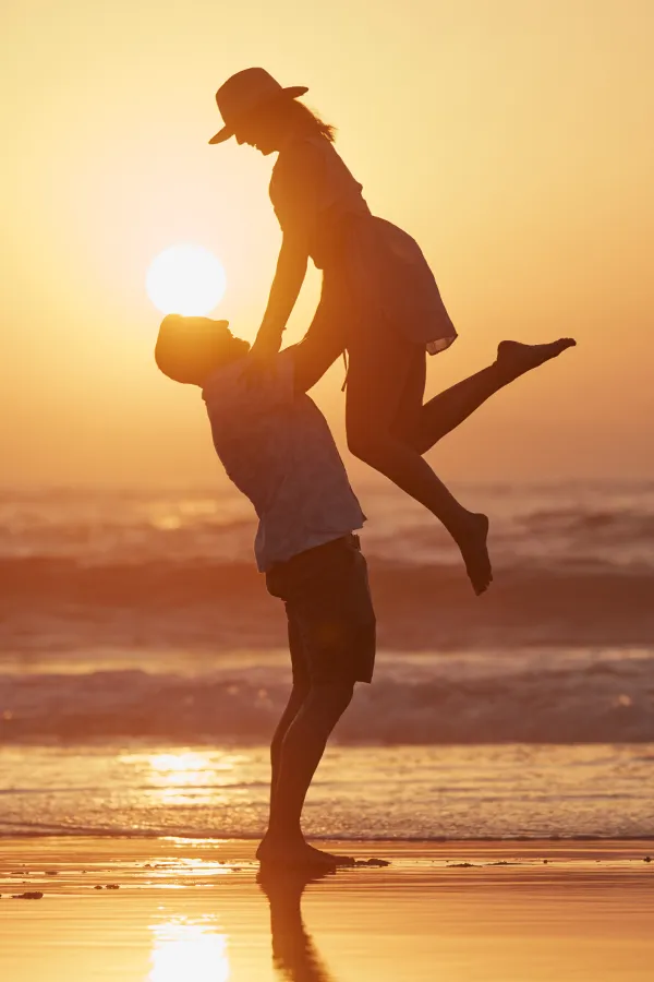 Myrisk-Genetic-Cancer-Screening-Treatment A man lifts a woman up on the beach, framed by the sunset. Get Myrisk genetic cancer screening from Nonkulie Dladla, M.D. in Manhattan.