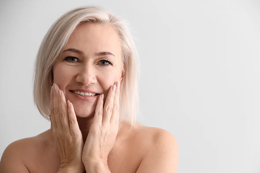 PRP-Microneedling-Clinic A mature woman touches her faces to feel the successful results of PRP microneedling and skin rejuvenation treatments from Nonkulie Dladla, M.D. in Manhattan.