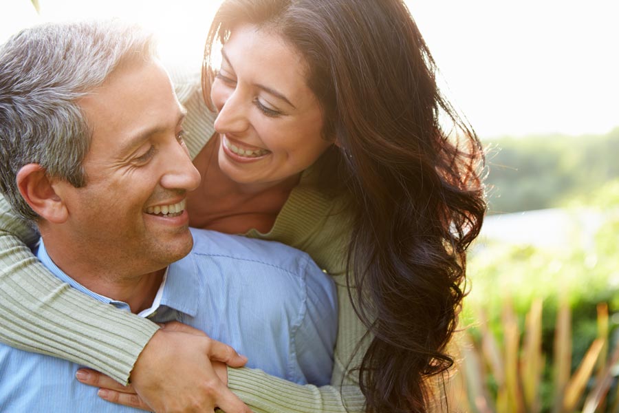 Regenerative-Exosome-IV-Therapy-Clinic A middle-aged latin couple embrace playfully in a green field. Get regenerative exosome IV therapy from Nonkulie Dladla, M.D. in Manhattan.