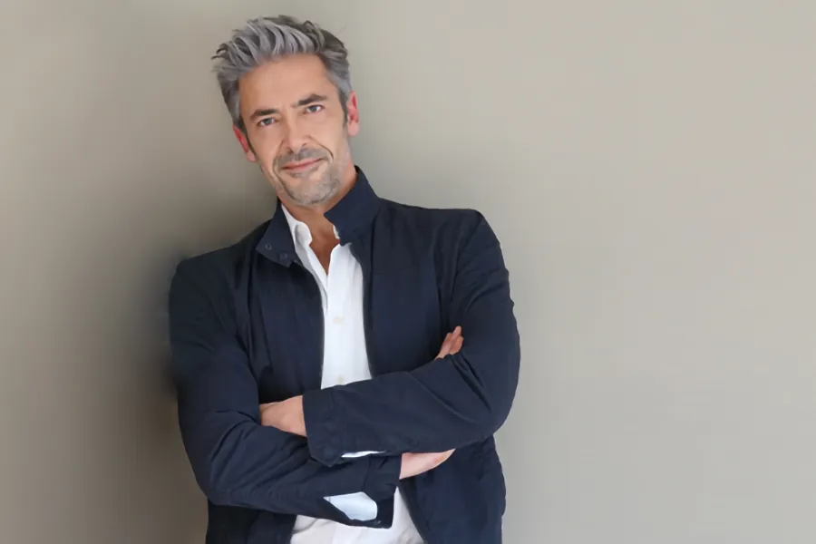 Testosterone-Low-T-Solutionsn-Clinic A middle-aged man in a white shirt and dark blue jacket leans against a gray wall smiling. Get testosterone for Low T from Nonkulie Dladla, M.D. in Manhattan.