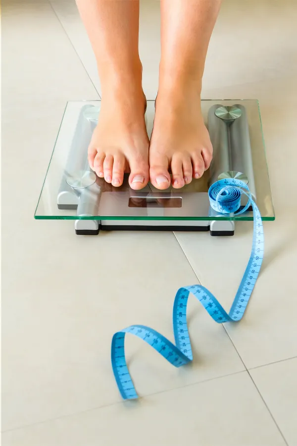 Weight-Loss-Resistance-Treatment Close-up of a woman's feet standing on a scale, with measuring tape by her toes, getting treatment for weight loss resistance from Nonkulie Dladla, M.D. in Manhattan.