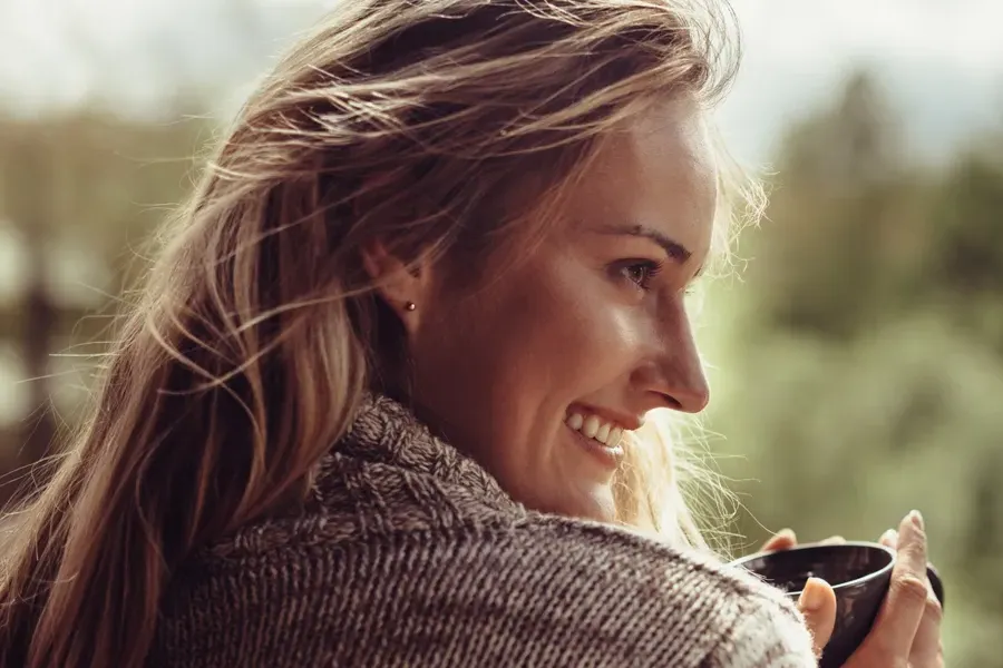Womens-Health-Exams-Clinic A middle-aged blonde woman in a sweater drinks tea, framed by a forest horizon. Get comprehensive women's health exams from Nonkulie Dladla, M.D. in Manhattan.